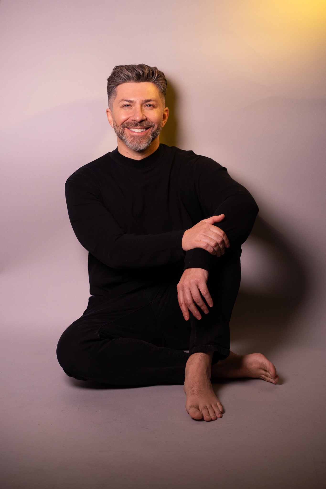 John Castaño sentado e sorrindo em retrato de corpo inteiro